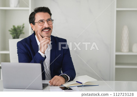 Thoughtful businessman in a blue suit with a charming smile looking upwards Thoughtful businessman in a blue suit with a charming smile looking upwards 112723128
