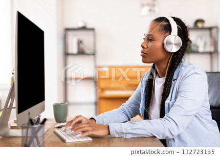 Focused black lady student with headphones works on computer for online class 112723135
