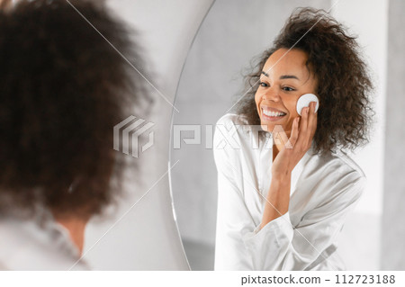 African woman takes care of skin with cotton pad indoor African woman takes care of skin with cotton pad indoor 112723188