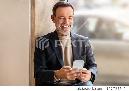 Smiling senior businessman in a stylish blazer using his smartphone 112723241