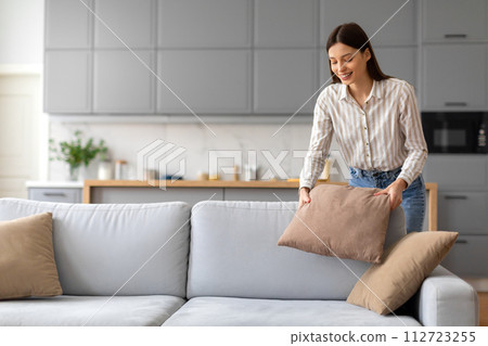 Smiling young woman arranging cushions on sofa 112723255