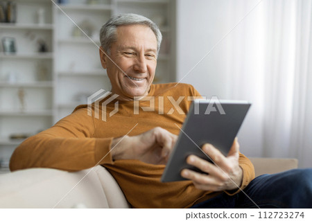 Happy senior man chilling at home, using tablet Happy senior man chilling at home, using tablet 112723274