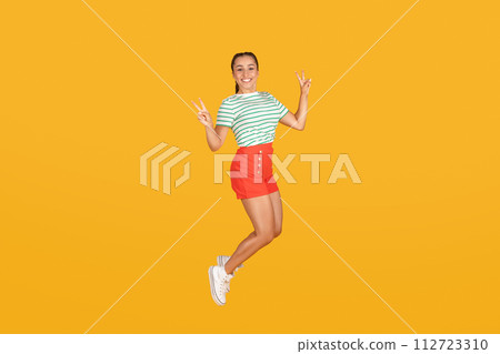 Cheerful young woman jumping over yellow background Cheerful young woman jumping over yellow background 112723310