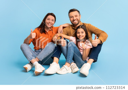 Cheerful parents and daughter making thumbs up gesture, blue background 112723314