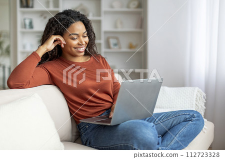 Smiling Black Female Relaxing With Laptop On Couch At Home Smiling Black Female Relaxing With Laptop On Couch At Home 112723328