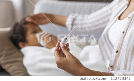 Black mother touching son's forehead and checking his temperature with digital thermometer Black mother touching son's forehead and checking his temperature with digital thermometer 112723341