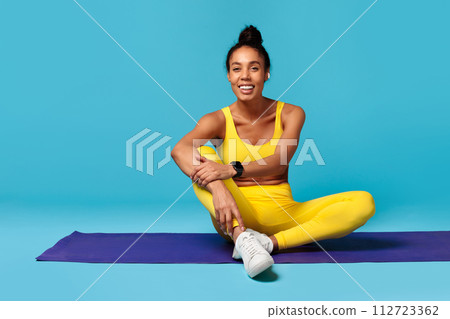 black lady in activewear with tracker sits on mat, studio 112723362