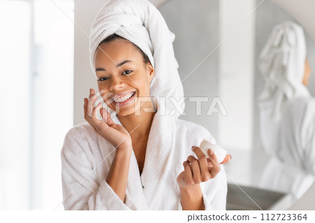 Portrait of black lady posing with cream jar in bathroom Portrait of black lady posing with cream jar in bathroom 112723364