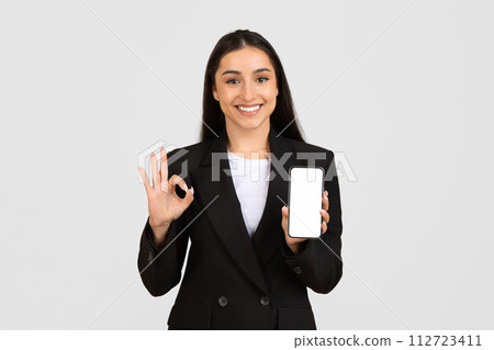 Happy businesswoman with blank phone showing OK sign Happy businesswoman with blank phone showing OK sign 112723411