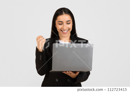 Joyful young businesswoman with laptop celebrating success 112723415