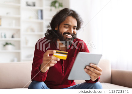 Cheerful indian man using digital tablet and bank credit card Cheerful indian man using digital tablet and bank credit card 112723541