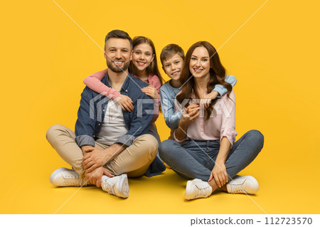 Happy young family of four sitting on floor and embracing 112723570