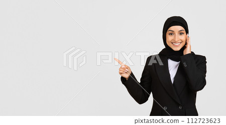 Smiling muslim businesswoman in hijab pointing to the side at free space 112723623