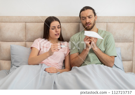 Worried couple with thermometer and tissue in bed 112723737