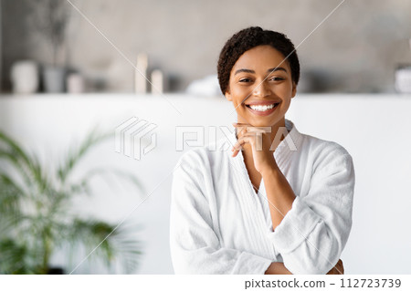 Attractive young black woman in white bathrobe standing in bathroom 112723739