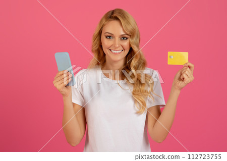 Happy blonde woman holding smartphone and credit card, pink background 112723755