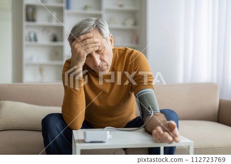 Unhealthy senior man using an upper arm blood pressure monitor 112723769