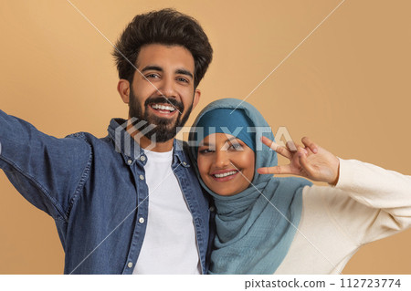 Happy Young Muslim Couple Taking Selfie Together Against Beige Background 112723774