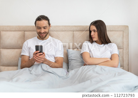 Man smiling at cellphone, woman sitting upset beside him Man smiling at cellphone, woman sitting upset beside him 112723793