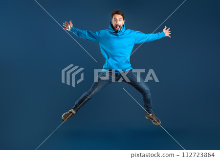 Crazy Offer. Funny Young Man Jumping Like A Star Over Blue Background Crazy Offer. Funny Young Man Jumping Like A Star Over Blue Background 112723864