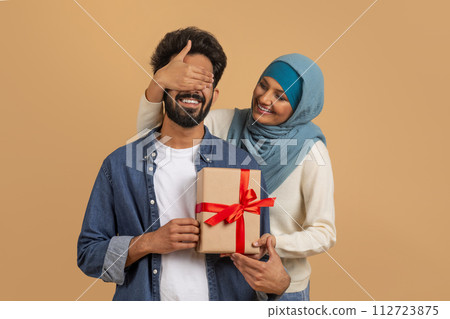 Surprise for you. Romantic muslim woman covering husbands eyes and giving present Surprise for you. Romantic muslim woman covering husbands eyes and giving present 112723875