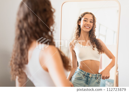 teen girl looks at mirror satisfied with weight loss indoor teen girl looks at mirror satisfied with weight loss indoor 112723879