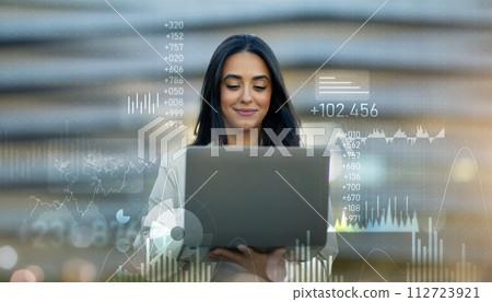 Confident young professional woman using a laptop, overlayed with dynamic financial charts 112723921