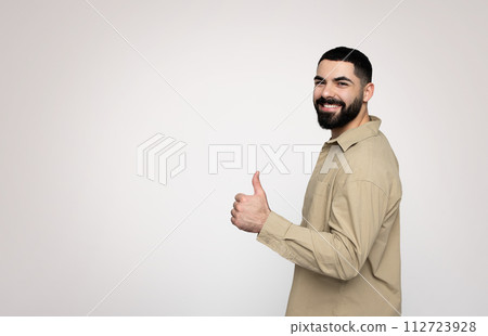 Side profile of a smiling bearded man in a beige shirt giving a thumbs up sign 112723928