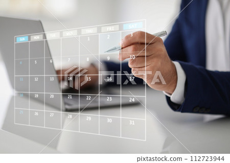 Close-up of a businessman's hand with a pen pointing to a transparent digital calendar 112723944