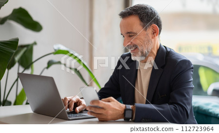Engaged senior businessman multitasking with a laptop and smartphone 112723964