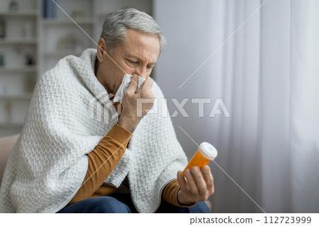 Sick elderly man sneezing and holding jar with pills Sick elderly man sneezing and holding jar with pills 112723999