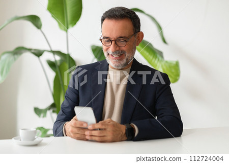 Cheerful senior businessman in a smart blazer browsing on his smartphone 112724004