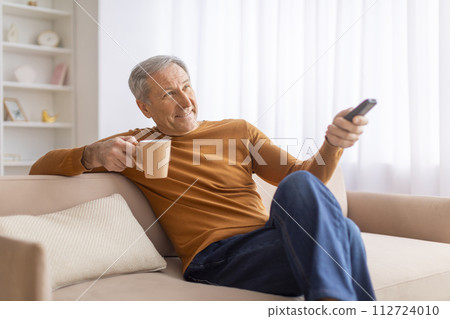Cheerful senior man reclining on couch at home 112724010
