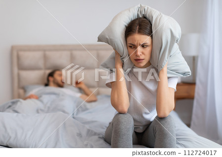 Woman frustrated by snoring, covering ears with pillow 112724017