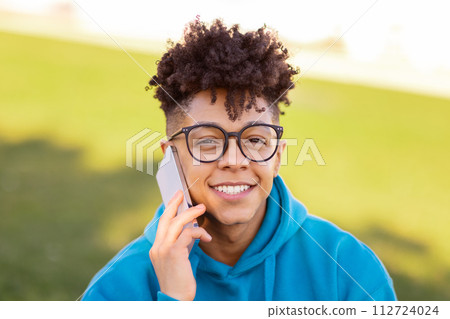 Portrait of smiling black student guy talking on cellphone outdoors Portrait of smiling black student guy talking on cellphone outdoors 112724024