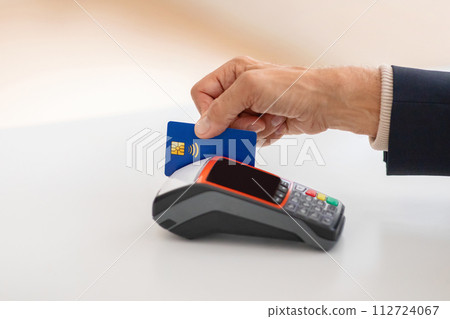 Close-up of a hand presenting a blue contactless credit card over a modern payment terminal 112724067