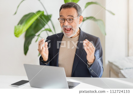 An exuberant middle-aged businessman with glasses joyfully reacts during a video call An exuberant middle-aged businessman with glasses joyfully reacts during a video call 112724133