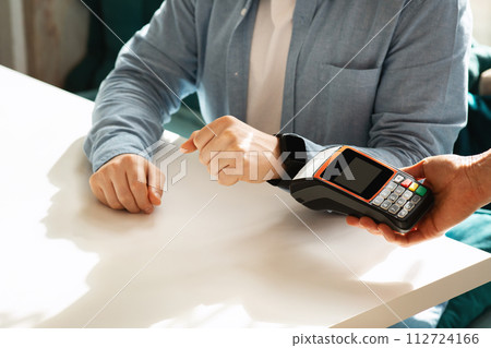 Close-up of a person's hands completing a contactless payment using a smartwatch at a point of sale terminal Close-up of a person's hands completing a contactless payment using a smartwatch at a point of sale terminal 112724166