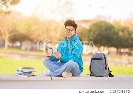 Brazilian university student enjoying coffee and using his smartphone outdoor 112724170