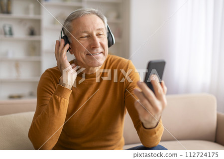 Positive elderly european man using headphones and cell phone 112724175