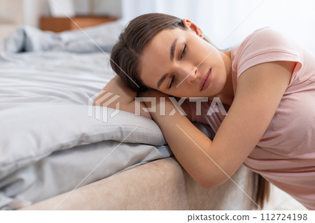 Exhausted young woman resting in bed, showing signs of sleep deprivation or illness 112724198
