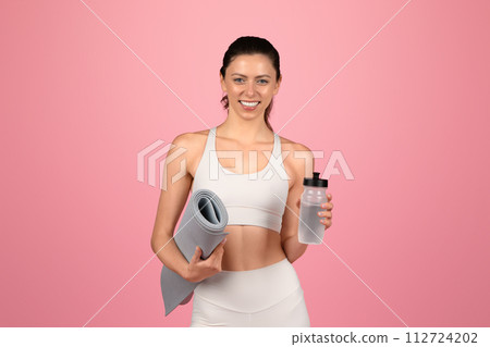 Happy and healthy young woman with a yoga mat and a water bottle in hand 112724202