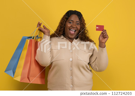 Excited chubby black lady with purchases and credit card 112724203