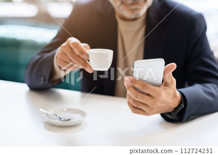 Close-up of a man's hands as he multitasks with a white espresso cup in one hand 112724231