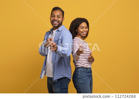 Cheerful young black couple playfully pointing at the camera with confident smiles 112724268