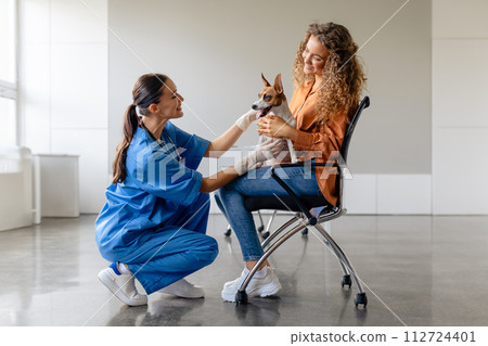 Vet kneels to greet dog in owner's lap at clinic 112724401