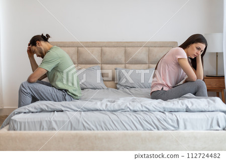 Upset couple sitting apart on bed, facing away Upset couple sitting apart on bed, facing away 112724482