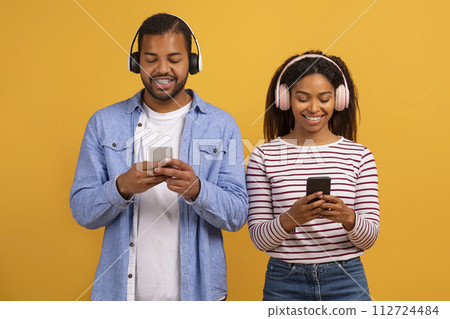 Smiling Black Couple Wearing Wireless Headphones Using Modern Smartphones Smiling Black Couple Wearing Wireless Headphones Using Modern Smartphones 112724484