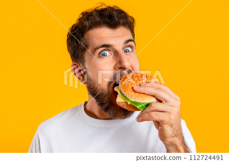 funny guy satisfying food cravings with cheeseburger on yellow background 112724491