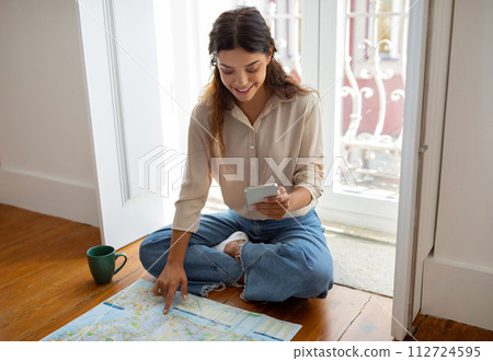 Young woman using her smartphone and city map to plan journey Young woman using her smartphone and city map to plan journey 112724595